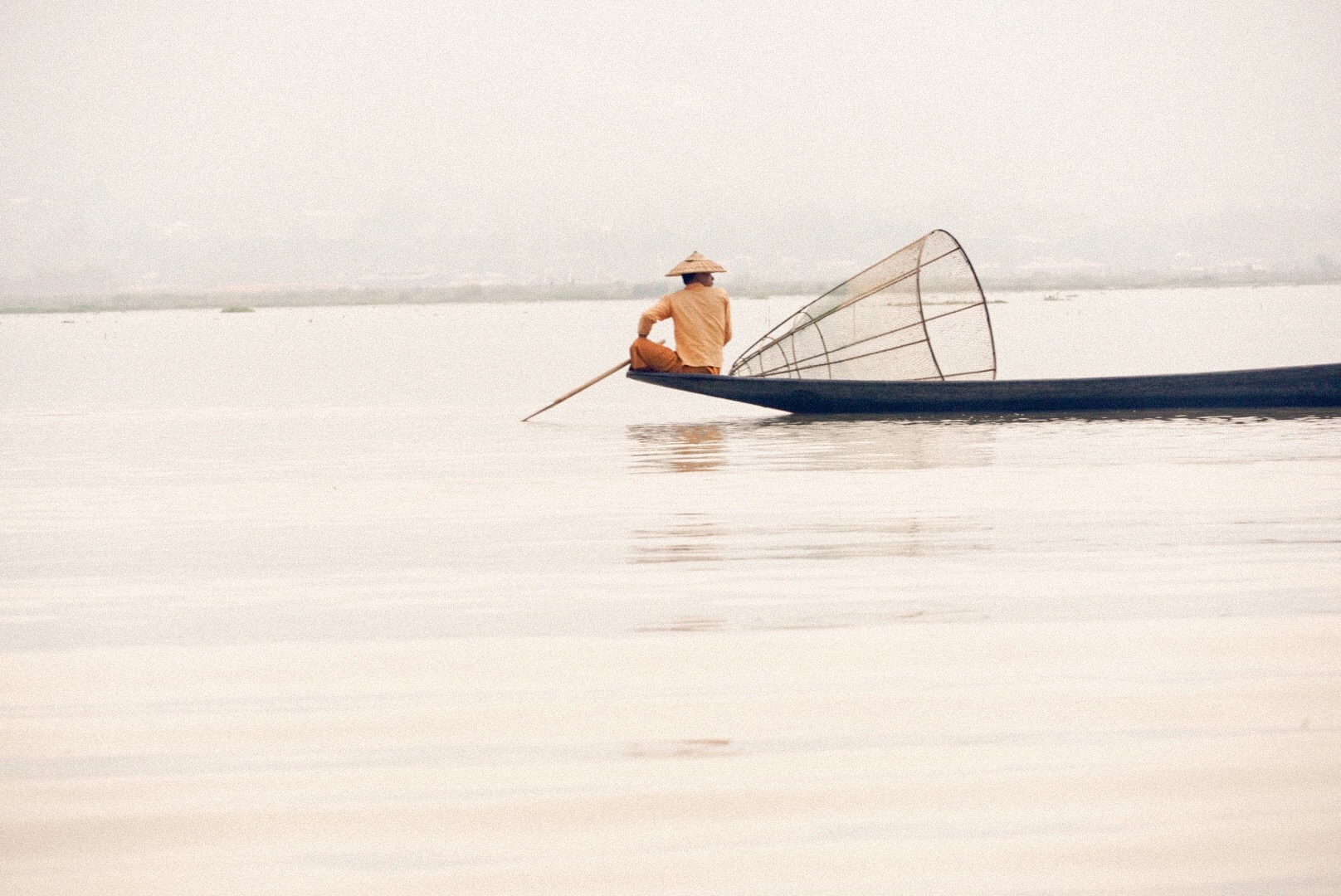 Fisherman on his boat with a conical fish trap on Inle Lake