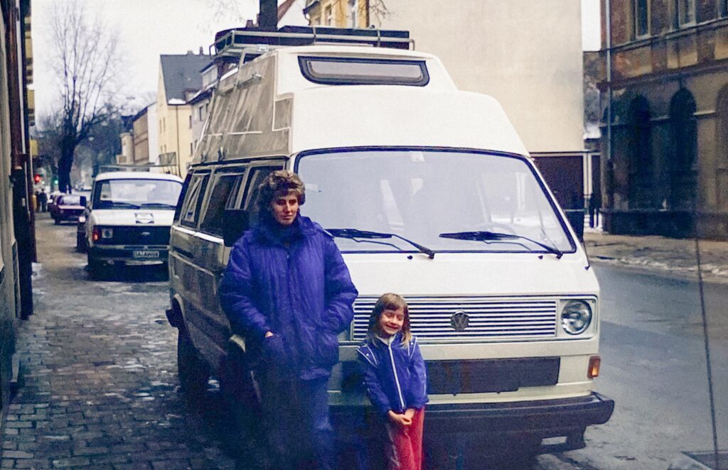 Child and mother in front of a VW camper van at the start of a family road trip, 1987